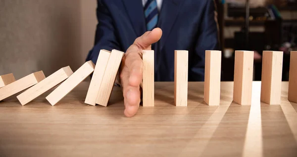 Businessman hand Stopping Falling wooden blocks. Dominoes effect. Strategy and successful intervention concept for business.