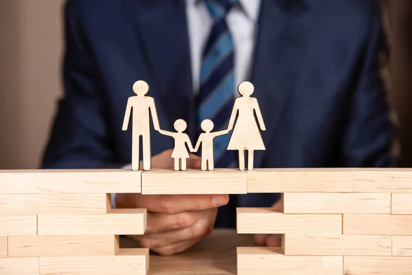 Takım elbiseli bir adam bir ailenin üzerinde durduğu sembolik bir köprüye sahiptir. Hayat sigortası kavramı.