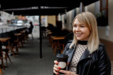 Şehir kafesinde oturan ve gülen ceketli güzel ve genç bir kız. Yaz.