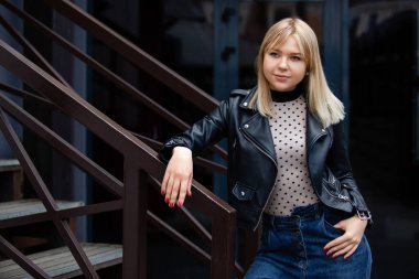 Açık hava yaşam tarzı portresi. Siyah ceketli, çekici, sarışın bir kız..