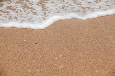 Deniz kıyısına yakın çekim. Islak kumun üzerindeki bir dalgadan beyaz köpük. Su hattına odaklan, arka planlar için doğal doku.