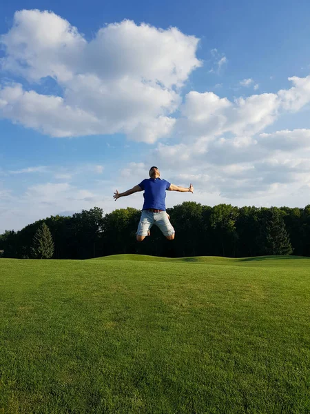 A man in a jump with outstretched arms between sky and land