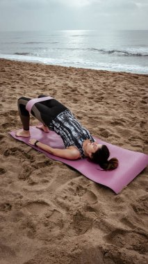 Genç ve güzel bir kadın sahilde antrenman yapıyor.