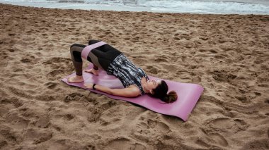 Genç ve güzel bir kadın sahilde antrenman yapıyor.