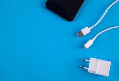 Mavi arka planda izole edilmiş beyaz şarj aleti ve akıllı telefon..