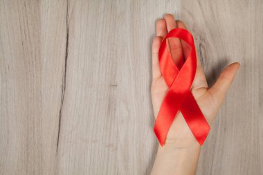 Kırmızı kurdele - HIV 'li yaşayanlar için farkındalığın ve desteğin sembolü, ahşap arka plan, kadın eli.