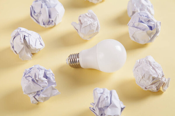 Creativity inspiration. Light bulb and crumpled paper balls on yellow background.