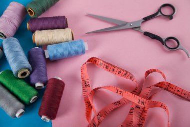İplikler, makas ve örgü bandı, pembe ve mavi arka planda izole edilmiş.. 