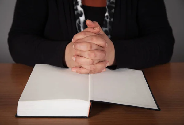 Woman hands praying with a bible in a wooden table.