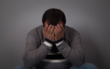 Üzgün adam elleri yüzünde, gri arka plan. 