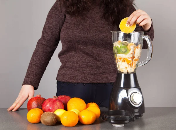 Blender, woman, fruits and gray background.