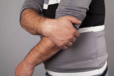 Dirsek ağrısı çeken bir adam. Gri arkaplan. 