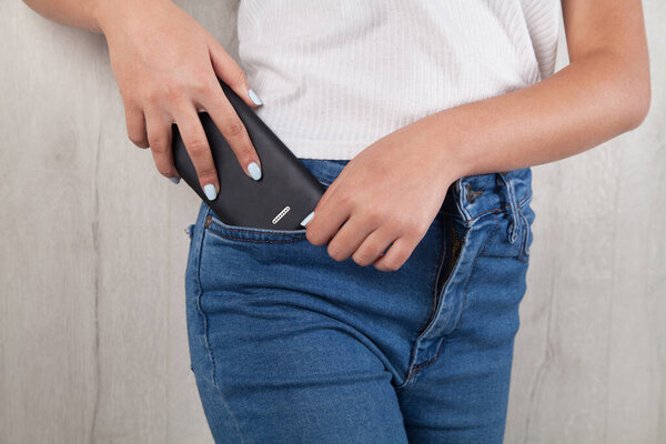 Женщина кладет мобильный телефон в карман.