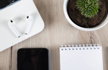 Akıllı telefon, kablosuz kulaklık, defter ve ahşap arka plandaki aksesuarlar..