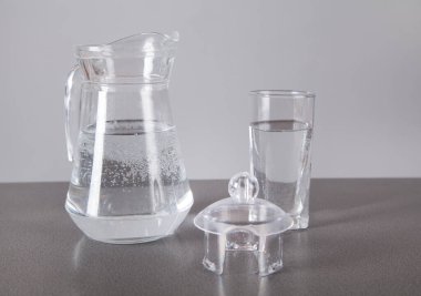 Gri arka planda, su dolu bardak ve sürahi..