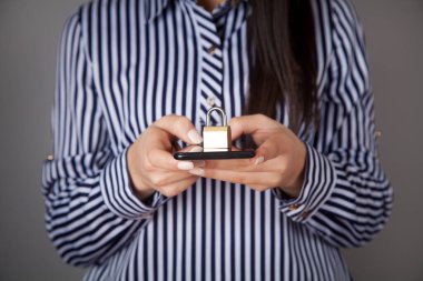 Beyaz kadın elinde bir asma kilit ve telefon tutuyor..