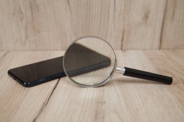 İzole edilmiş ahşap arka planda akıllı telefon ve büyüteç.