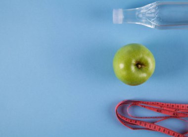 Ölçüm bandı ve mavi arka planda izole şişe ile tam yeşil elma.