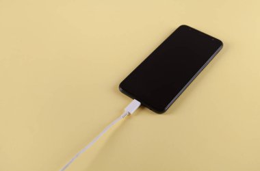 Sarı arka planda şarj olan mobil akıllı telefon.