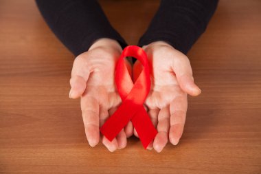 Kırmızı kurdele - HIV 'li yaşayanlar için farkındalığın ve desteğin sembolü, ahşap arka plan, kadın eli.