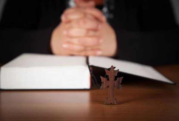 Woman hands praying with a bible and cross, wooden table.