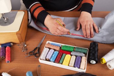 Kadın terzi dikiş makinesiyle çalışıyor. Elinde bir koli bandı var..