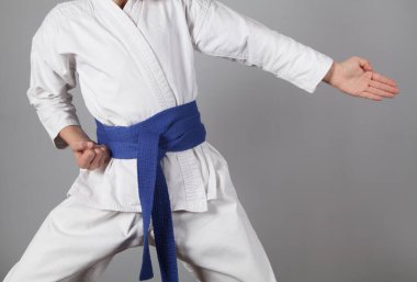 Gri arka planda karate eğitimi alan genç bir çocuk. Kimonolu çocuk..