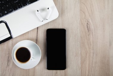 Akıllı telefon, kablosuz kulaklık, kahve ve ahşap arka planda aksesuarlar..