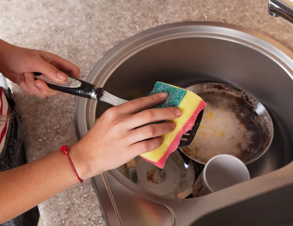 Genç bir kadın mutfakta bulaşıkları yıkıyor..