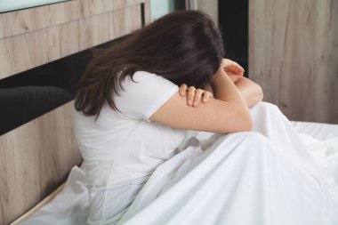 Yatakta acı çeken üzgün kadın. Yatakta oturan kadın üzgün görünüyor..