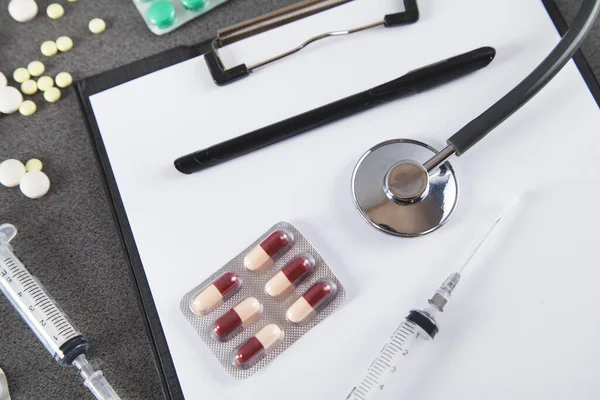 Doctors desk. Stethoscope, notebook and  pills, on gray background. Concept of medicine.