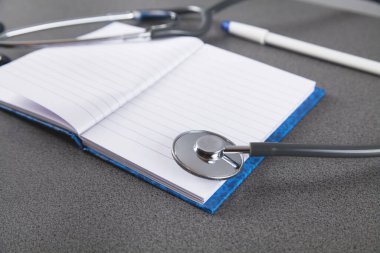 Gri arkaplanda steteskop, defter ve kalem. 