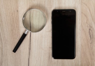 İzole edilmiş ahşap arka planda akıllı telefon ve büyüteç.