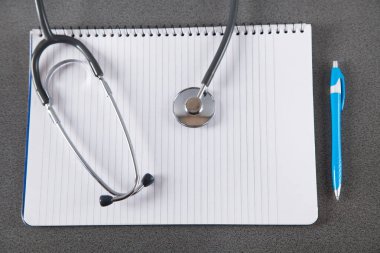 Gri arkaplanda steteskop, defter ve kalem. 