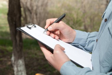 Kafkasyalı bir adam dokümanlara kalemle yazar. Açık havada..