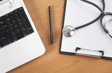 Stetoskop, bilgisayar, defter ve tahta arka planda kalem. Doktor masası..