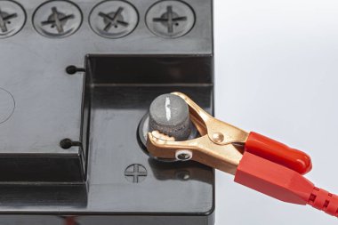 Kırmızı bir timsah klipsi siyah bir araba aküsünün pozitif terminaline bağlanır, elektrik bağlantısını ve güvenli güç transferini gösterir, otomotiv elektriksel görevlerindeki anahtar uygulamaları gösterir