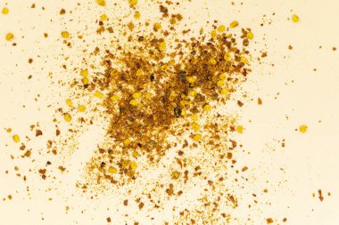 Açık bej bir yüzeye saçılmış ezilmiş kırmızı, turuncu ve sarı baharat renklerini gösteren ezilmiş kırmızı biber taneleri ve tohumların yakın plan görüntüsü..