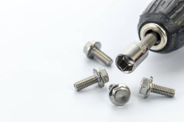 Temiz beyaz bir yüzeye saçılmış birkaç parlak çelik cıvatayla çevrili matkabın soket anahtarının yakın çekim görüntüsü, aletler ve donanım.