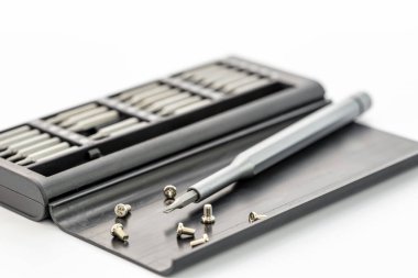 Gri tornavida ve çeşitli vidalar, beyaz arka planda birden fazla sürücü parçasının bulunduğu siyah bir kutuya yerleştirilmiş. Olay yeri iyi aydınlatılmış, detaylı ve odaklanmış.. 