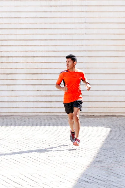 Young man running outdoors, vertical moving photograph, light background and orange clothing.