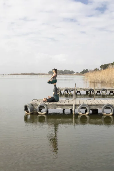 Couple practicing acroyoga in nature, a lake and a wooden dock