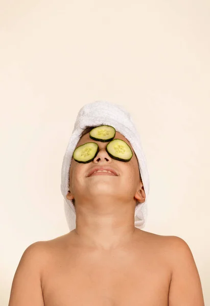 Child relaxes on a spa day. Child with towel on head and cucumber on face. Children\'s concept, skin care and relaxation.