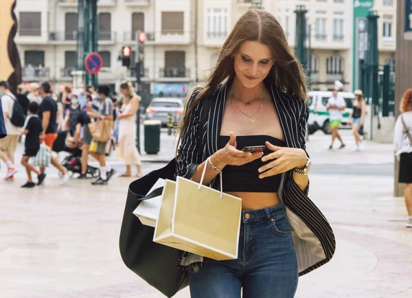 Young Caucasian woman with cell phone in hand walking through the city. Medium shot, horizontal image