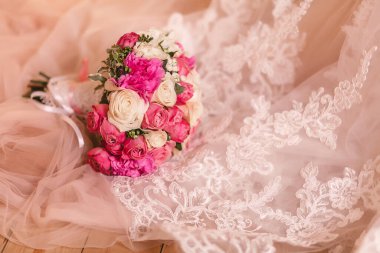 Gelinin elbisesinin kenarları aydınlık zeminde duruyor. Üzerinde süsler, nakış ve güzel bir buket var. Gelinin sabahının detayları..