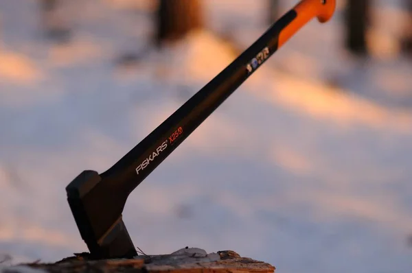 En fiskars yxa sitter fast i en stock. Vinterfiske med yxa för att hugga ved. En vass och praktisk yxa hugger ett träd mot en bakgrund av snö och solstrålar. — Stockfoto