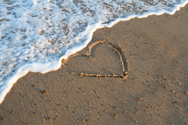 Heart handwritten on a sand of beach with wave. Background