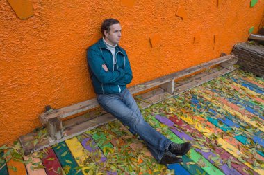 Düşen yapraklar arasında bir bankta oturan üzgün adam. İnsanlar