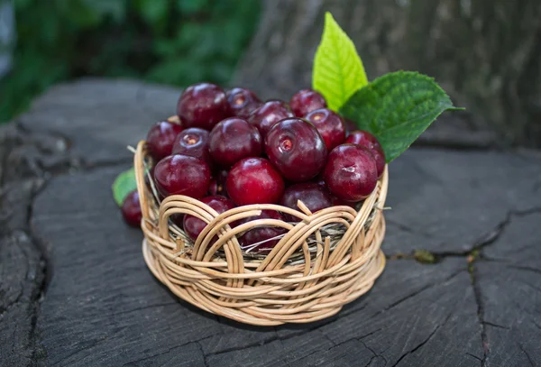 Cerezas maduras en una canasta de mimbre sobre un fondo de madera — Foto de Stock