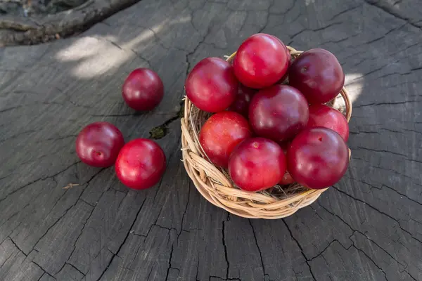 Ciruelas maduras en una canasta de mimbre sobre una superficie de madera. Fruta. — Foto de Stock